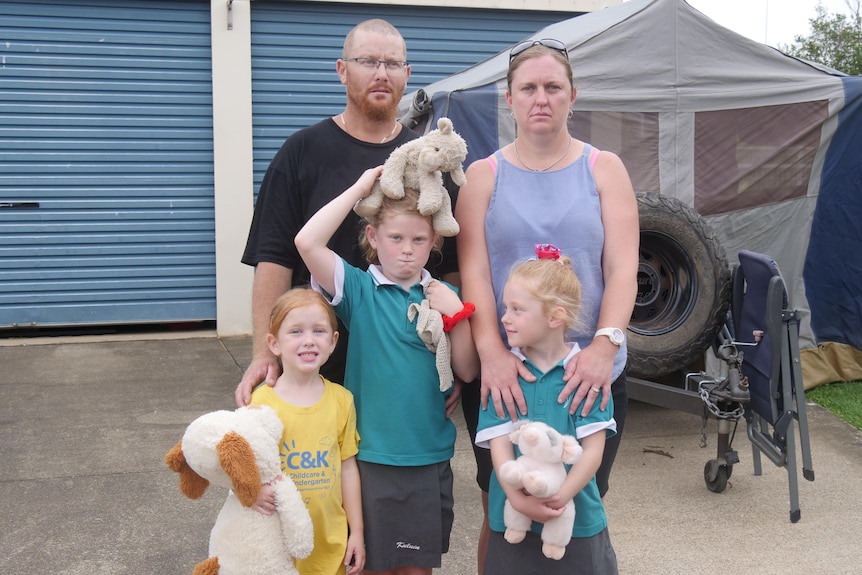 Parents and three kids stand in front of a caravan.