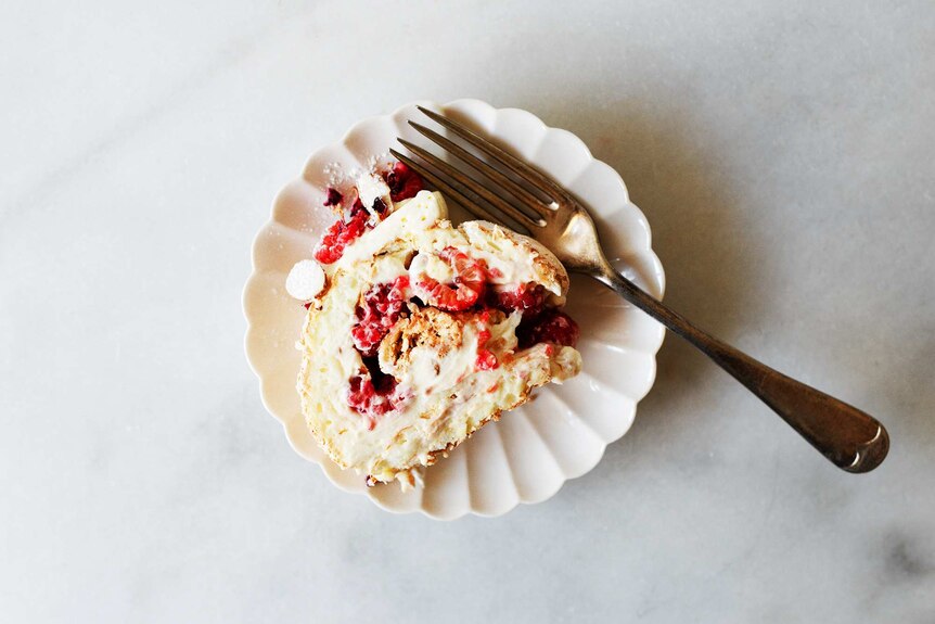 A slice of pavlova roll with raspberries and cream, ready to be served as dessert at a summer celebration.