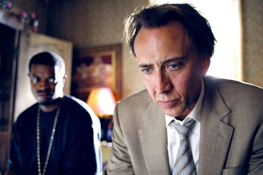 Colour still image of Nicholas Cage and Lucias Baston seated in a living room in 2009 film Bad Lieutenant.