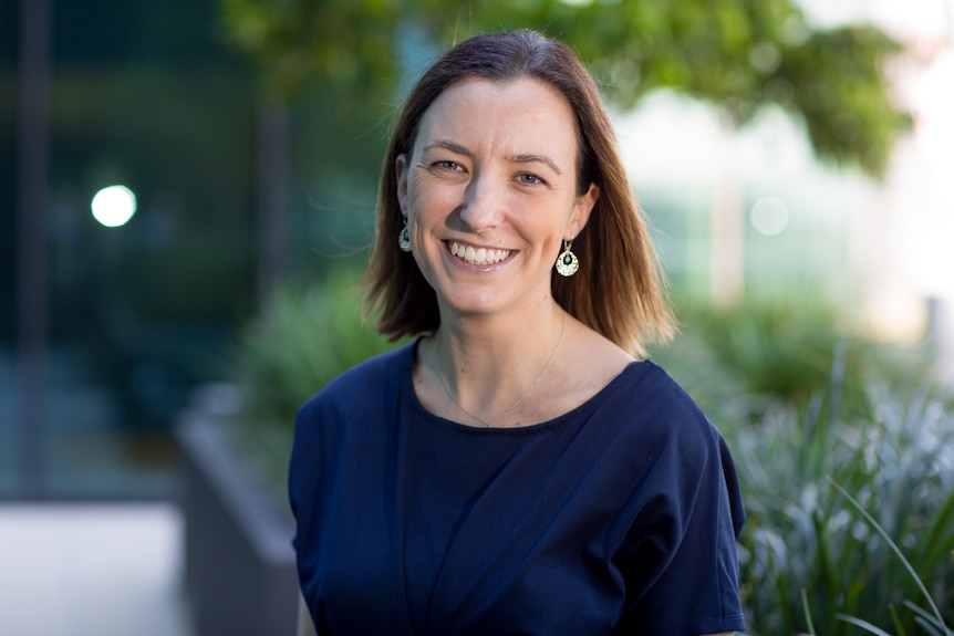 Sarah McNab smiles at the camera while outside with greenery behind her.