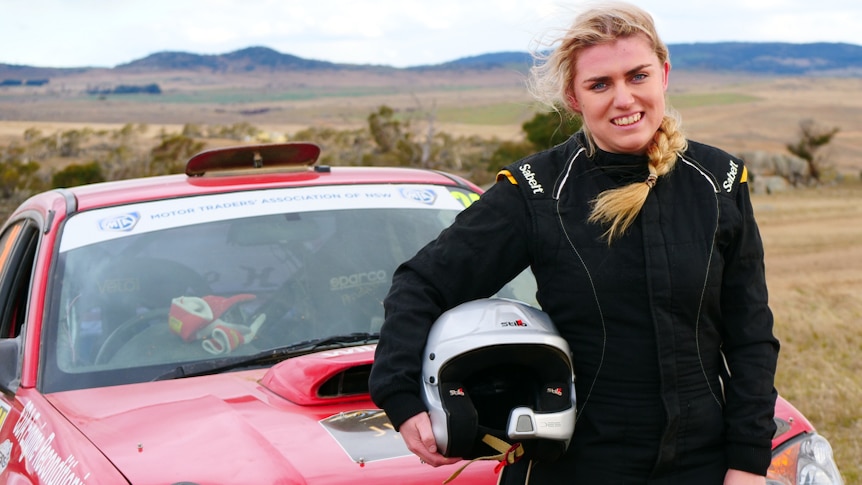 Portrait of young rally competitor standing at car holding her helmet
