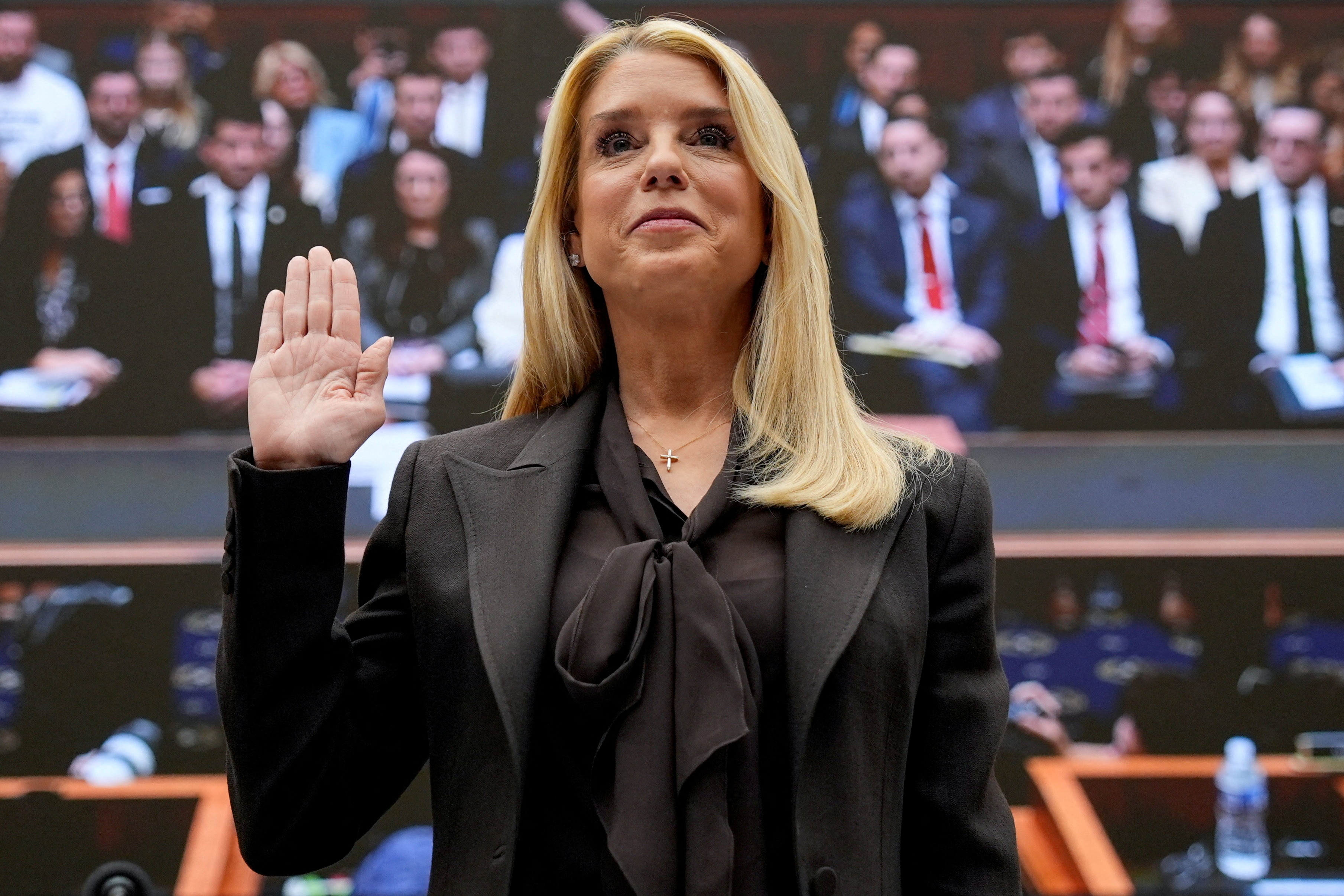 A woman in a black suit stands with her hand raised.