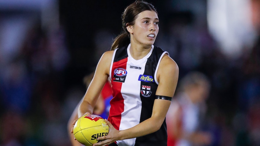 A St Kilda AFLW player holds the ball in two hands during a 2021 premiership match.