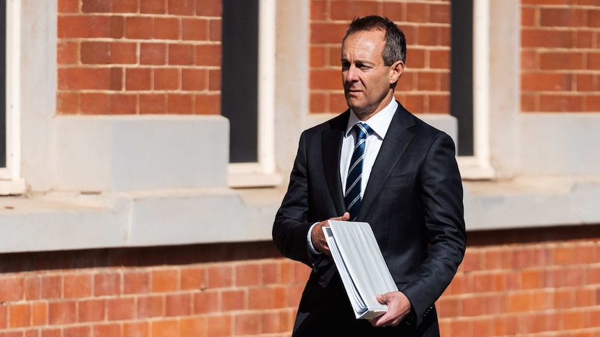 A man carries a folder outside a red brick building