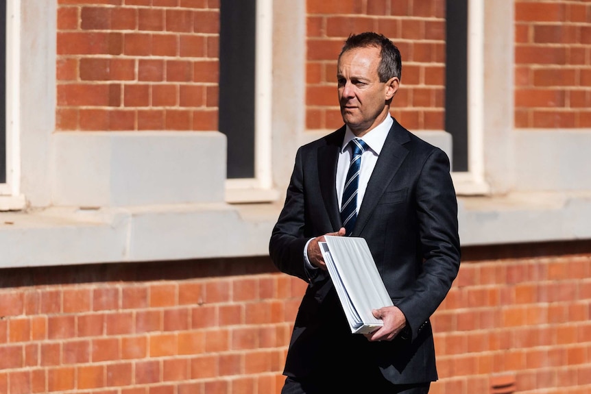 A man carries a folder outside a red brick building