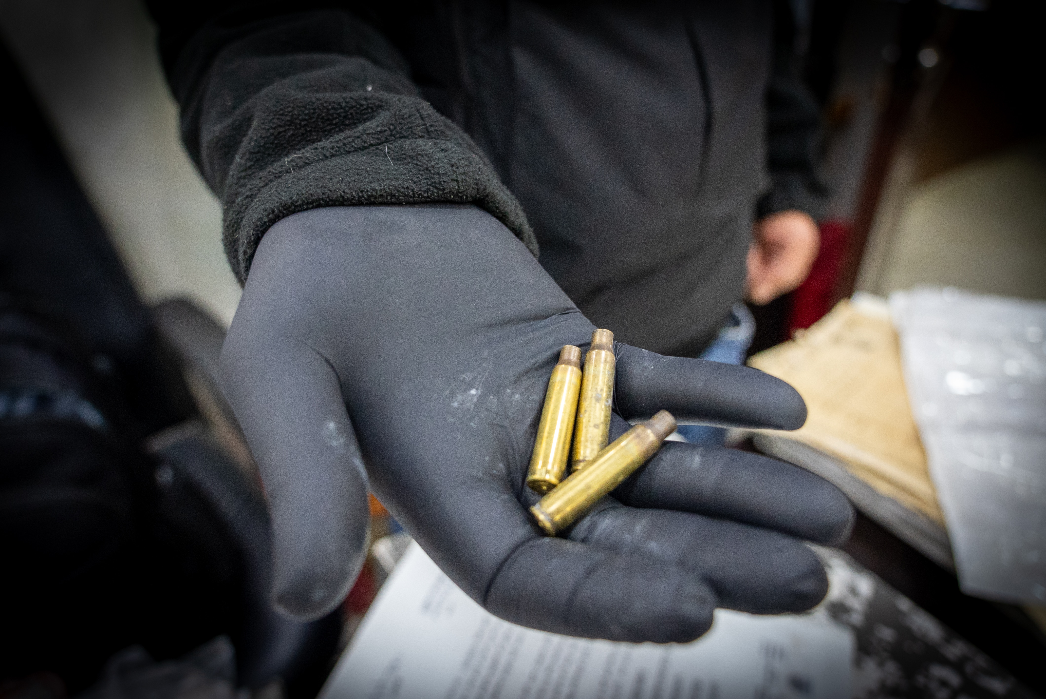 A man holds three shell casings in a gloved hand.