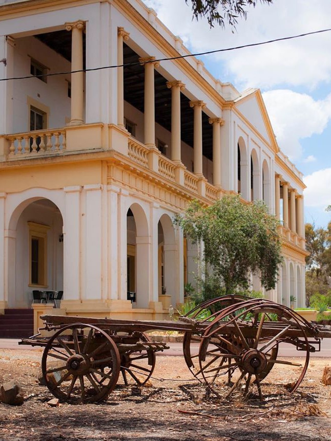 The old white and yellow New Norcia Hotel with a rusty horse wagon in front of it.