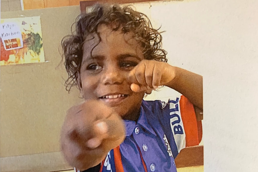 A young Aboriginal boy with curly hair wears a blue polo shirt