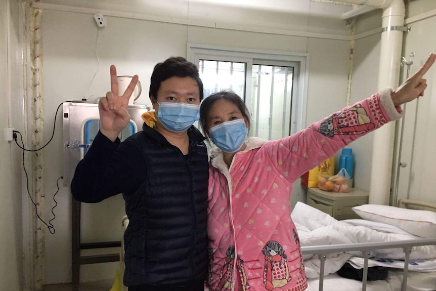 Wu Di and his mother-in-law wear masks and hold their hands in a peace sign in the air.