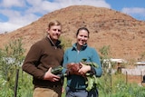 A couple standing in front of a crop with veggies in their hands.