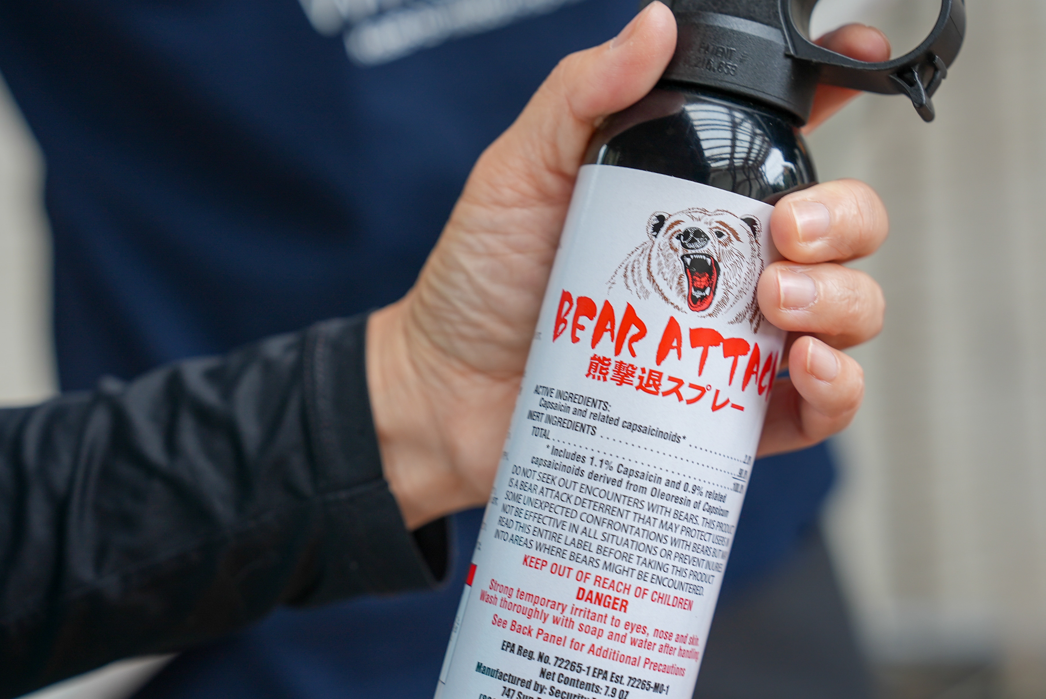 A hand on the trigger of a can that says 'bear spray' with a drawing of a bear growling