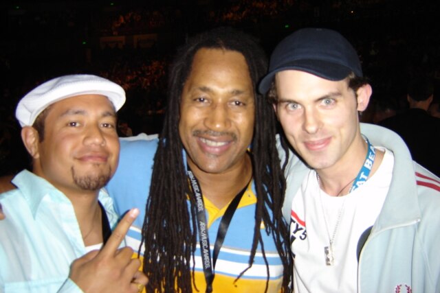 Three men smiling at the camera - DJ Kool Herc in the middle, flanked by the members of Koolism