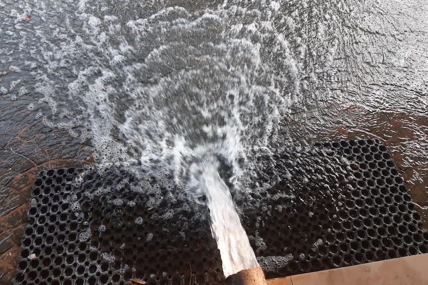 Water mixed with alcohol gushes onto a road from a pipe on the footpath.