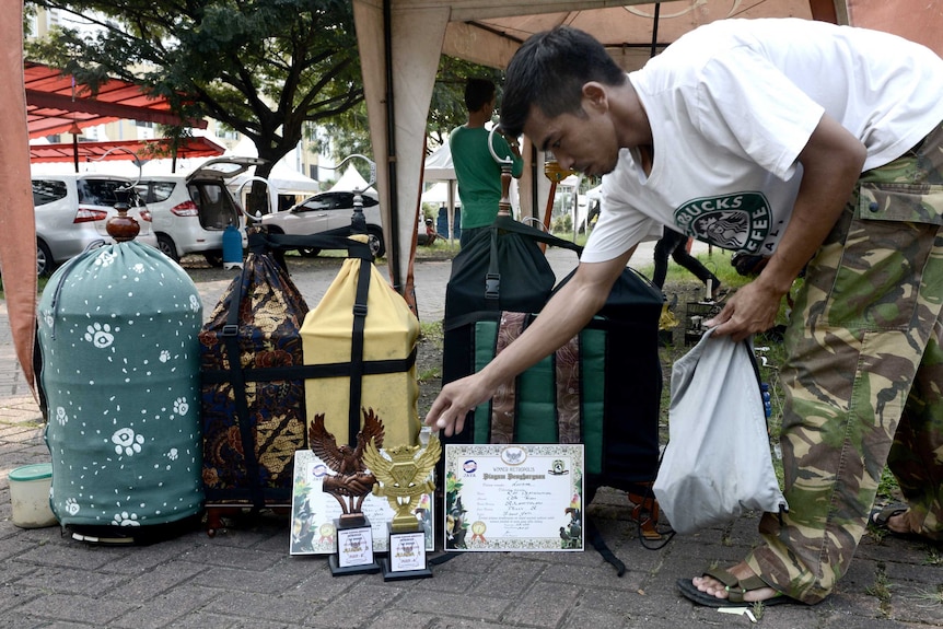 A bird enthusiast proudly showing off the trophies won by his songbirds after a contest in Jakarta.