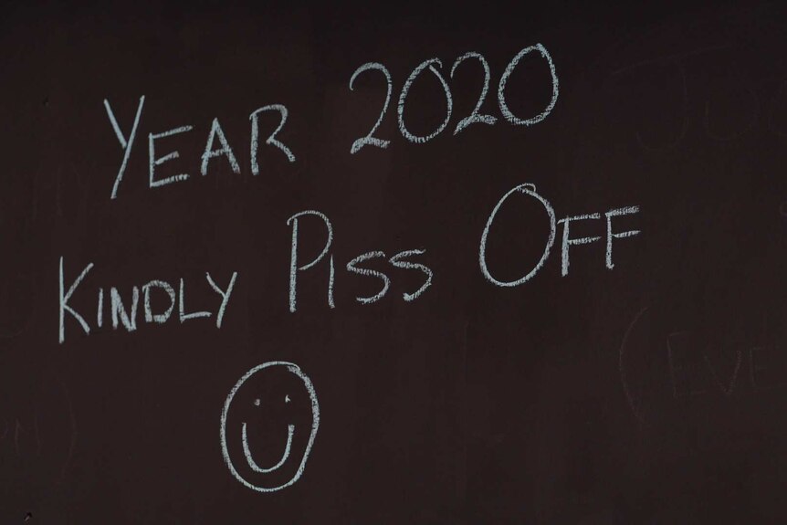 a black sign reads 'year 2020 kindly piss off' in white chalk