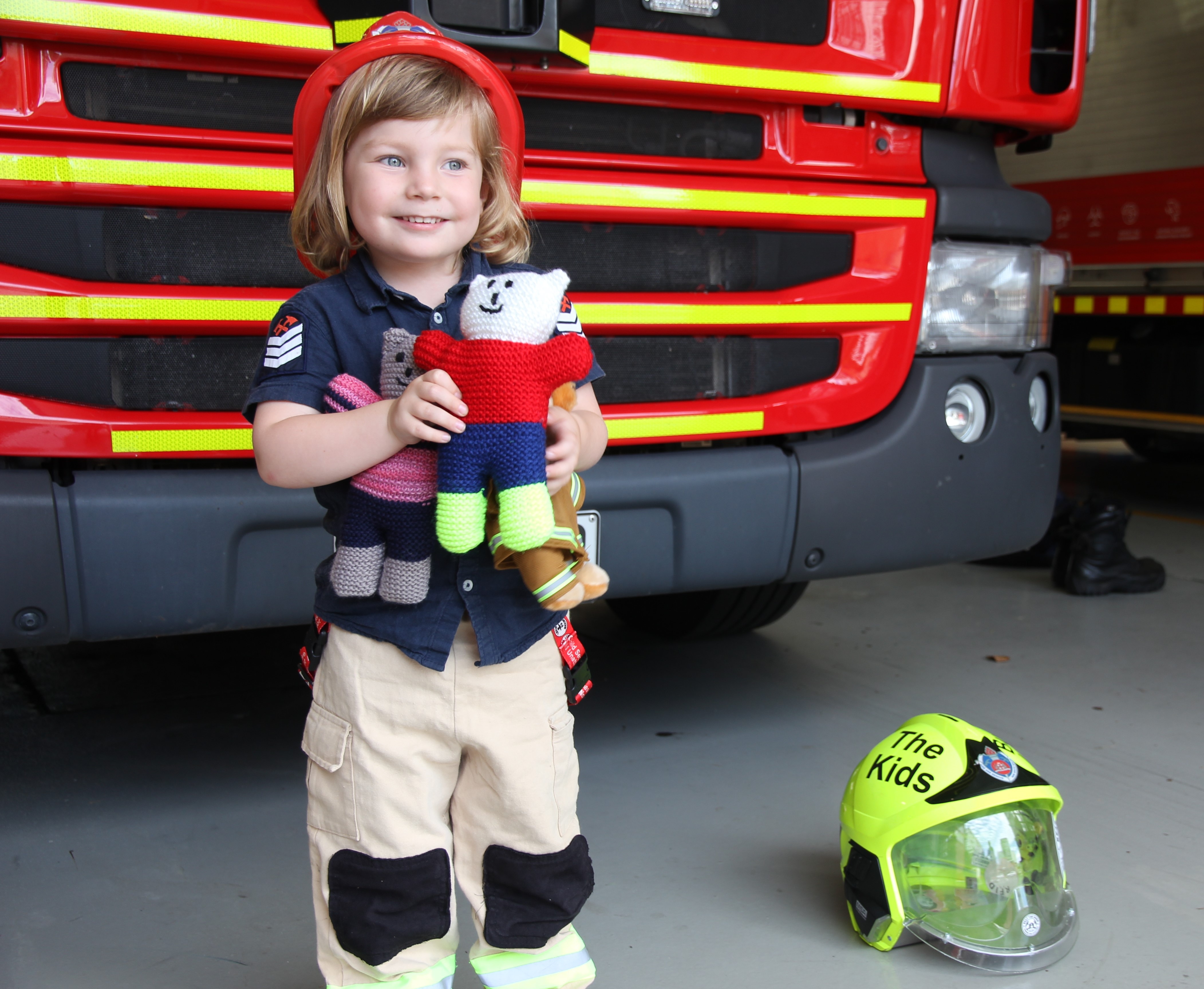 Liam Moffitt dressed in bright red helmet, custom-made firefighting uniform, holding trauma teddy 