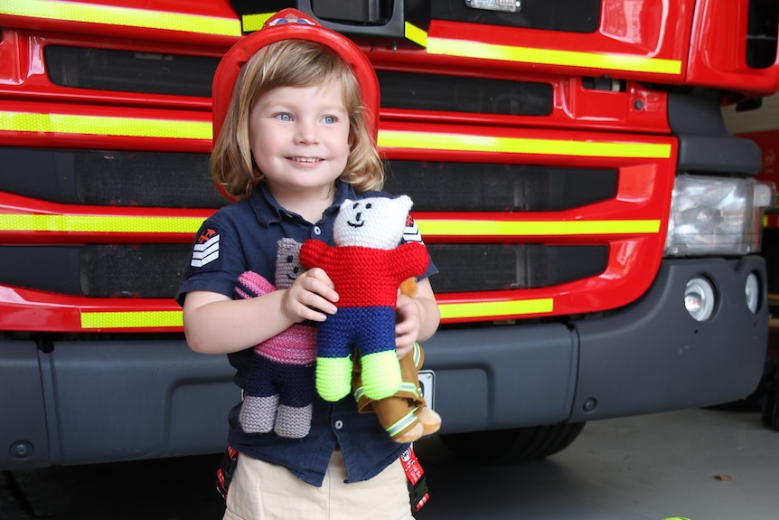Liam Moffitt dressed in bright red helmet, custom-made firefighting uniform, holding trauma teddy 