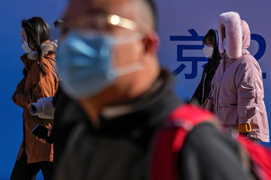 People wearing face masks walk in a shopping district of Beijing