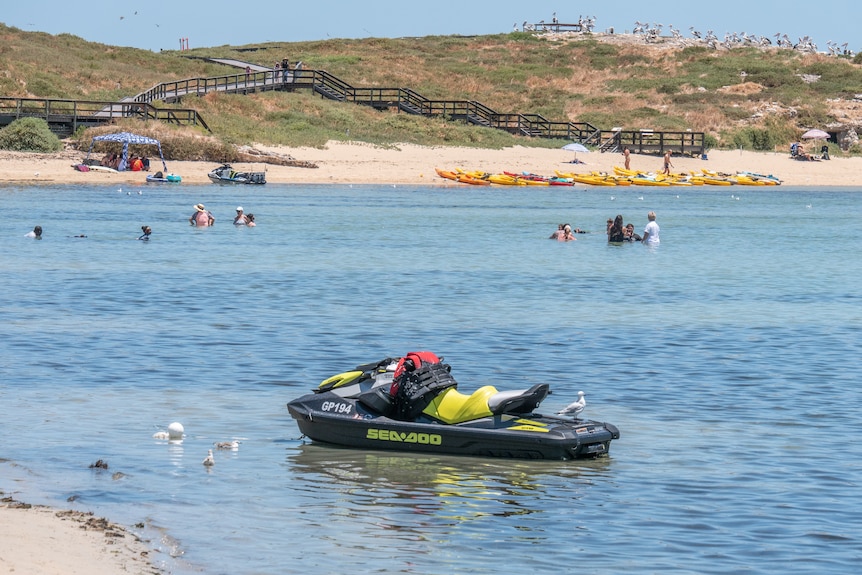 Swimmers and jetski in the water on the beach.
