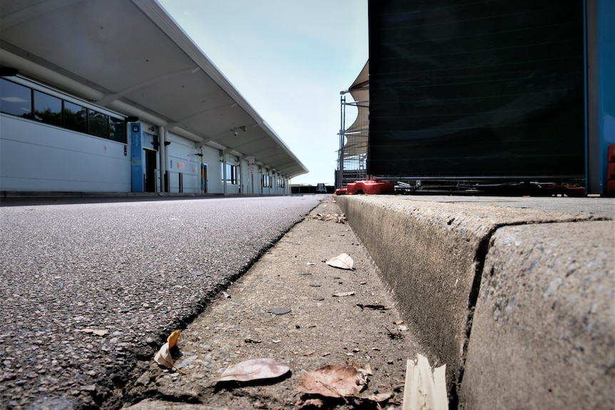 Street photo of a kerb and road showing a galvanised fence covered in black sheeting on the right and a building on the left.