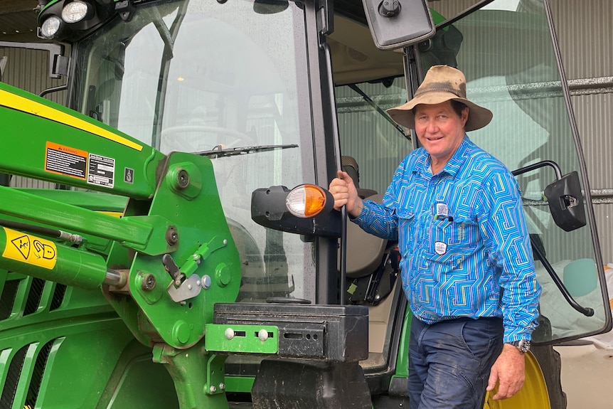 Carl Walker stands on the steps to his tractor holding onto the handle on the side 