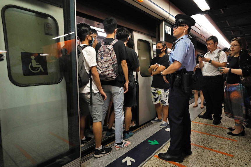A police officer stands on a subway platform in front of the doors of a train, which have been blocked by protesters.