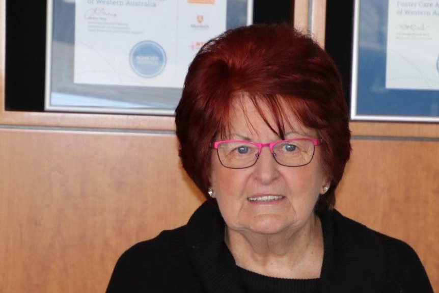 A woman wearing glasses standing in front of a wall with certificates in the back ground