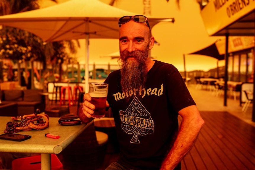 A man sitting with a beer amid an orange glow.