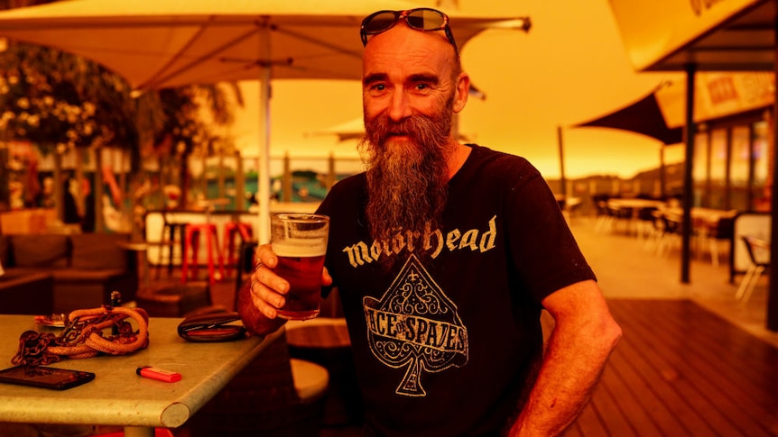 A man sitting with a beer amid an orange glow.