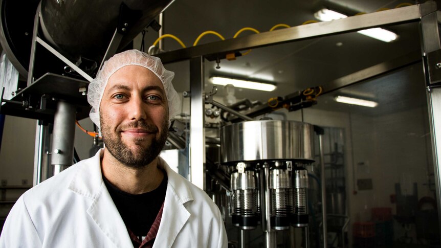 Simon Schulz stands in front of stainless steel dairy machinery.