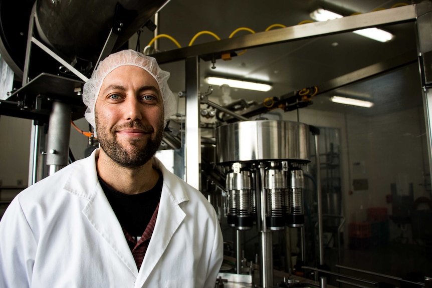Simon Schulz stands in front of stainless steel dairy machinery.