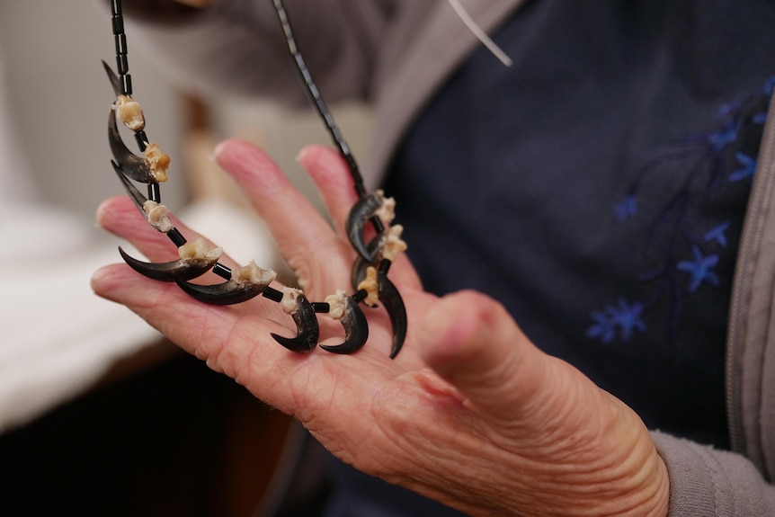 A close up of a woman's hand, holding a necklace made using eagle claws