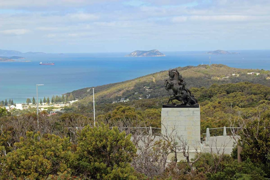 A wide shot of a statue of a horse overlooking a wide ocean harbour surrounded by hills.