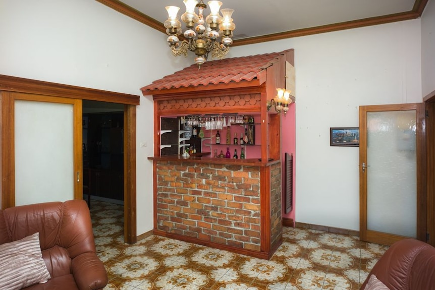 You're in a white-walled brown-tiled loungeroom with a mini-bar topped with terracotta pitched roof sitting in the corner.