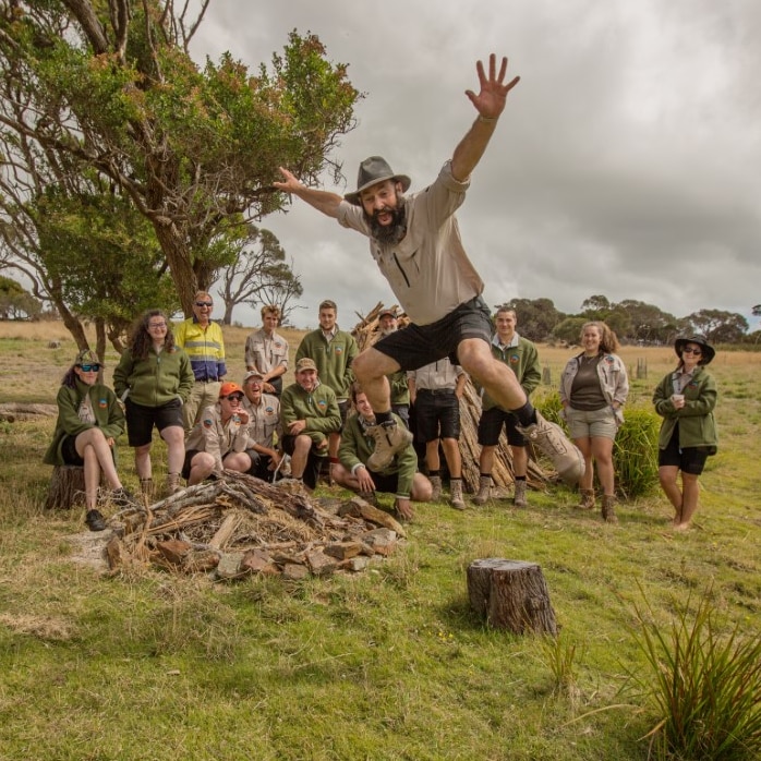 A man jumps in the air as a group sits on the grass behind him 