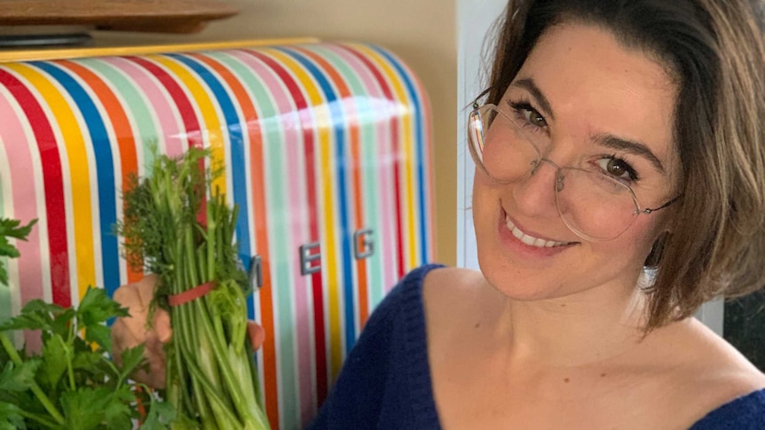 Food writer Alice Zaslavsky holds two bunches of herbs in front of her freezer, snap freezing to reduce food waste.-
