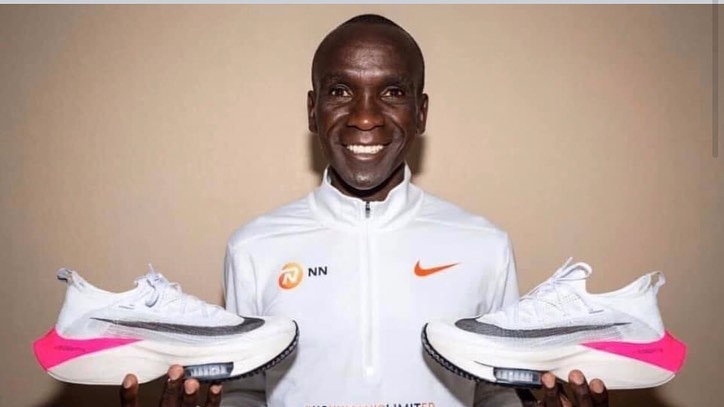 Marathon runner Eliud Kipchoge smiles as he holds his running shoes in his hands.