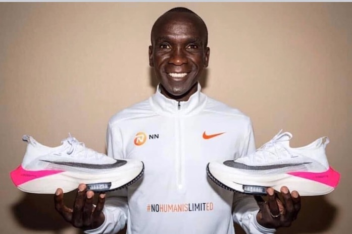 Marathon runner Eliud Kipchoge smiles as he holds his running shoes in his hands.