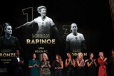 Podium of women's Ballon d'Or winner projected over a stage, with Rapinoe first, Lucy Bronze second and Alex Morgan third.