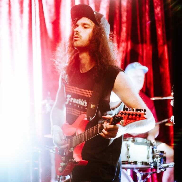 A photo of Chad Helman, a young man with long brown hair, playing a guitar on stage