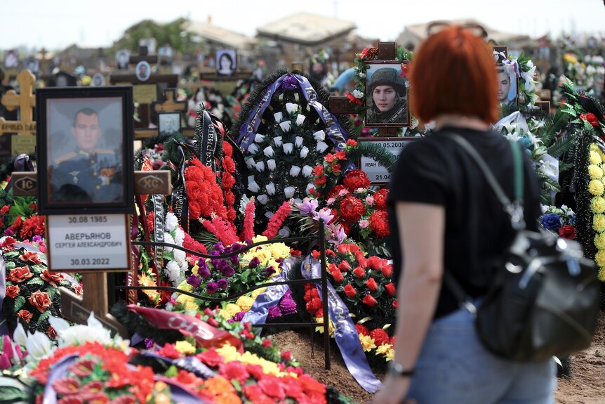 A woman at a Russian cemetery looks at the graves of Russian soldiers. They are covered in flowers. 
