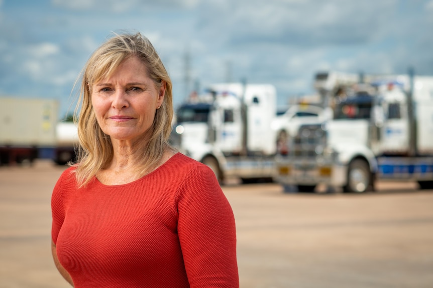a woman with blonde hair wearing a red shirt in front of trucks 