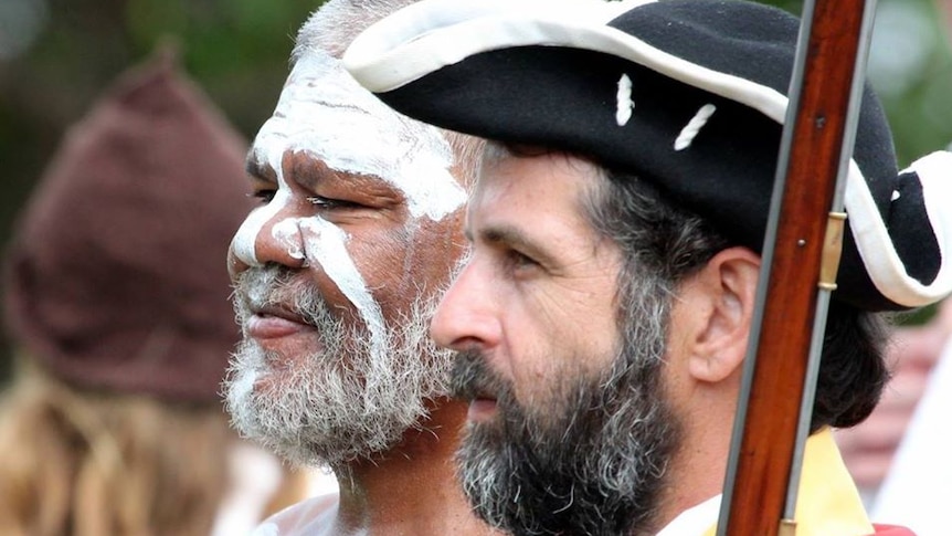 Close-up of faces of Aboriginal man with white paint on his face next to a Caucasian man wearing British navy uniform