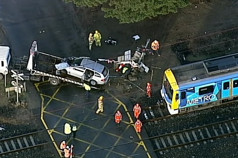 An aerial view of a emergency service workers standing near a stationary train and the wreckage of a car on a tow-truck.
