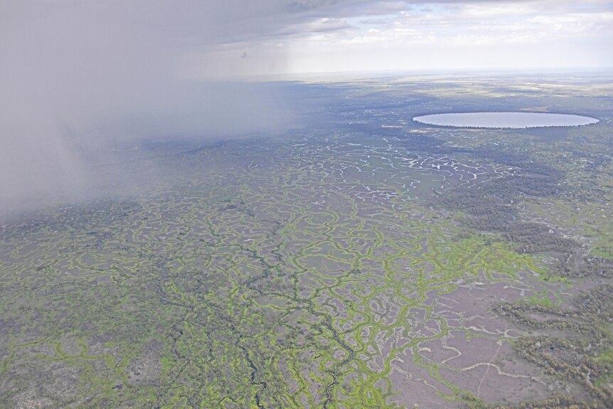 An aerial photo of rain clearing over green floodplains.