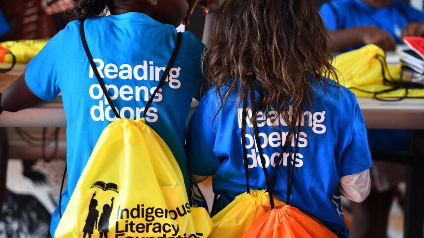 Two Indigenous children from the Milikapiti Community, Tiwi Islands wearing backpacks with the text, "Reading opens doors"