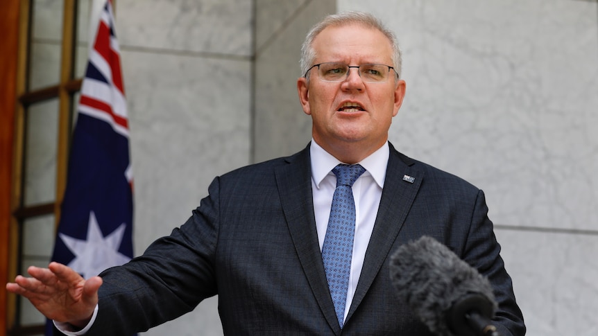 Scott Morrison with an outreached arm at a podium in the PM's courtyard