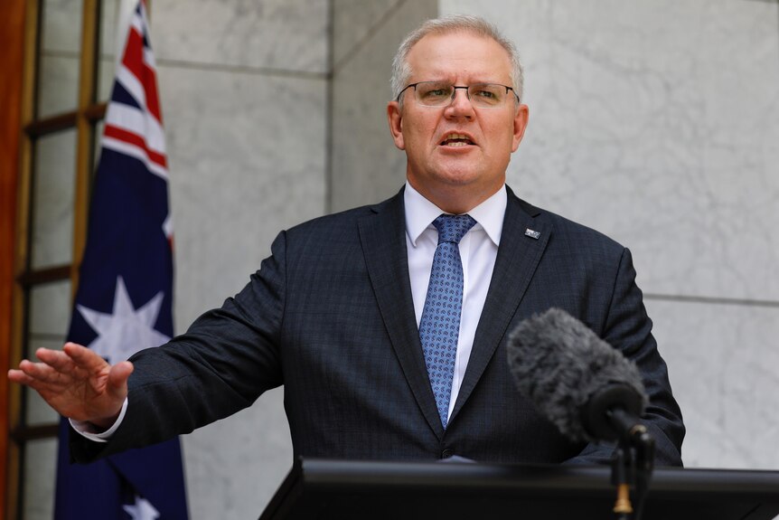 Scott Morrison with an outreached arm at a podium in the PM's courtyard