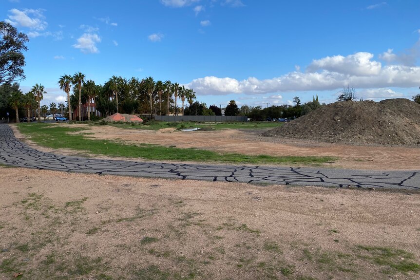 An open site with mounds of dirt and a bitumen track running through it.