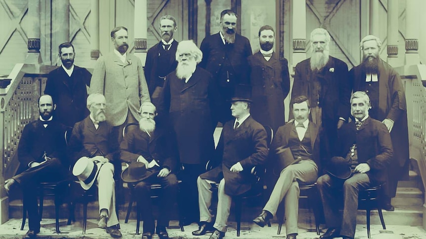 14 men dressed in suits pose for a photograph on steps in front of a building.